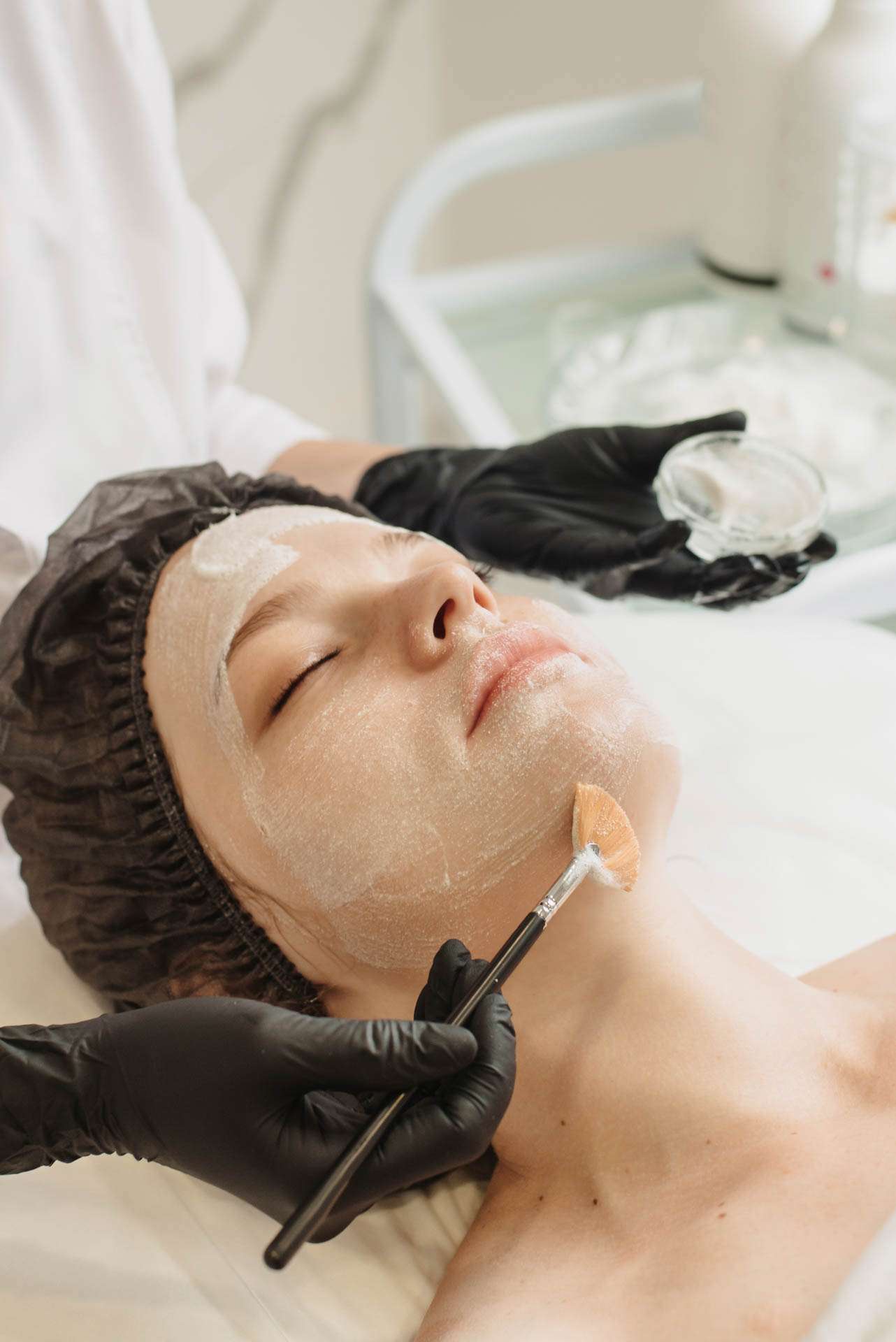 Facial peeling, spa treatments, skin care. A woman receiving facial care from a cosmetologist at a spa, close-up. Vertical photo