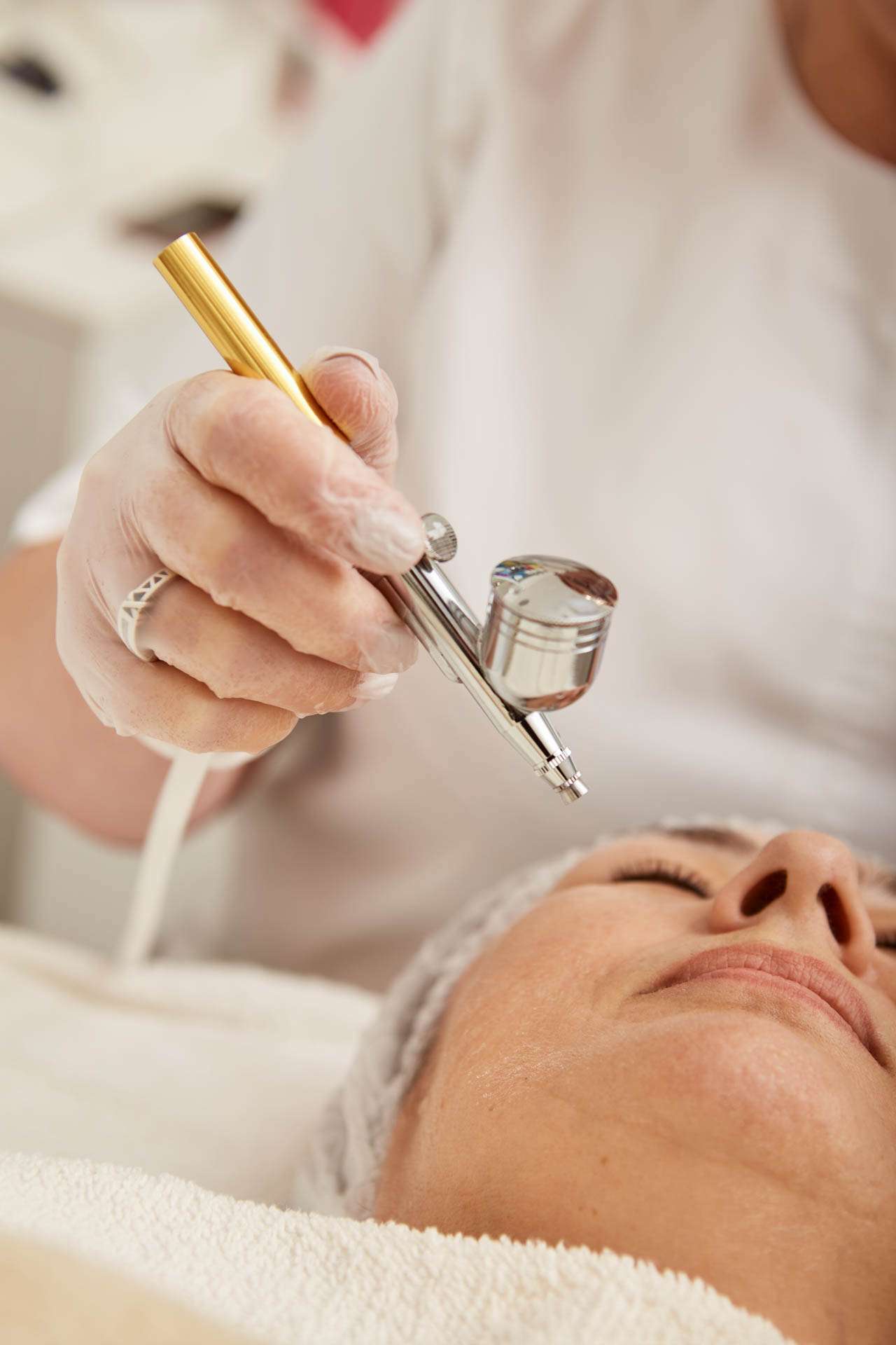 Close up of cosmetologist using oxygen mesotherapy device while female patient lying on daybed