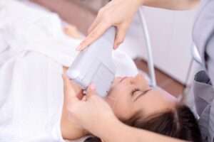 Portrait of relaxed young female client getting SMAS ultrasound face lifting massage